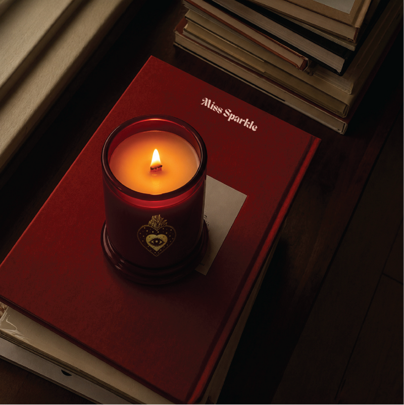 Lit Miss Sparkle candle resting on a red book
